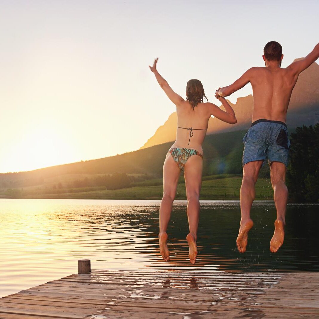 Taking the plunge. Rearview shot of a young couple in swimsuits leaping of a dock at sunset. Taking the plunge. Rearview shot of a young couple in swimsuits leaping of a dock at sunset.